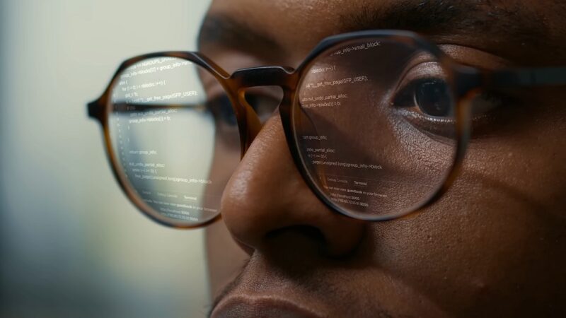 A guy programming with code reflecting in his glasses