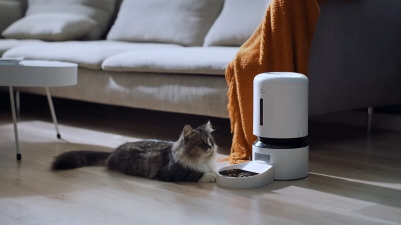 A cat lying on the floor near an automatic pet feeder in a modern home setting