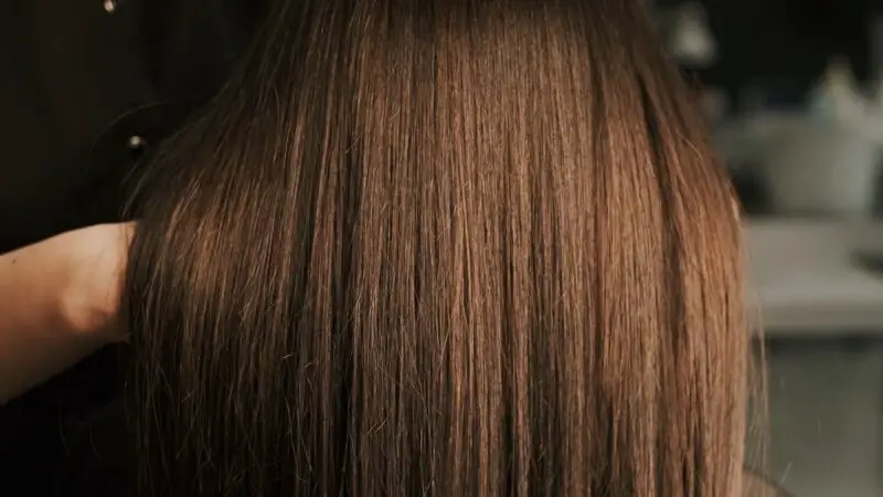 A close-up of long, straight, silky brown hair being handled by a stylist in a salon setting