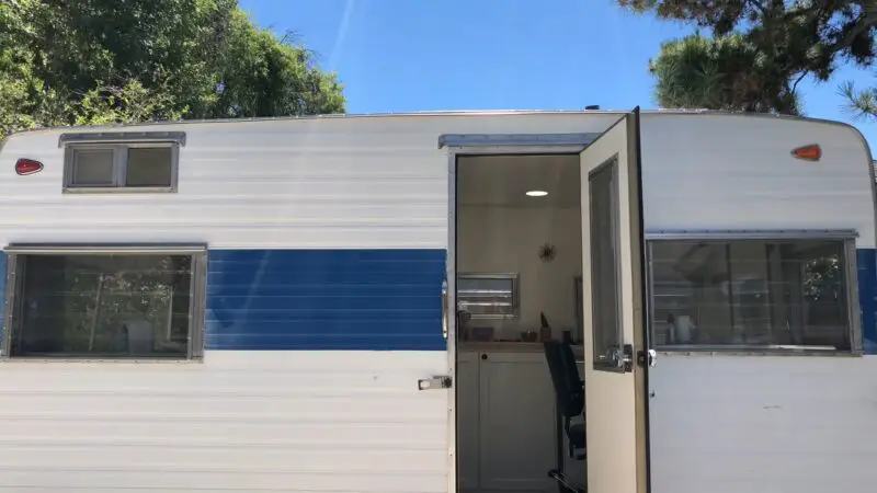 A vintage mobile salon with an open door revealing a clean, modern interior equipped with a styling chair and hairdressing tools